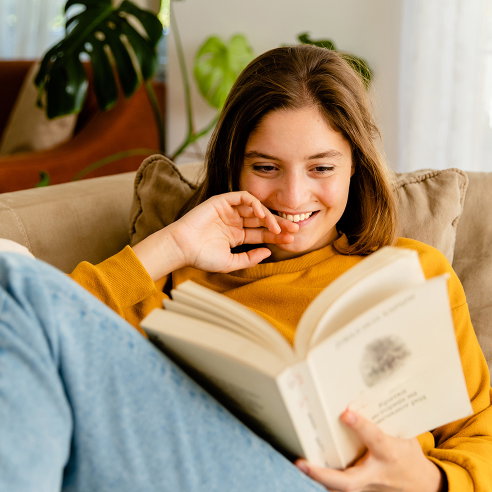 Young woman relaxing on sofa at home and reading book