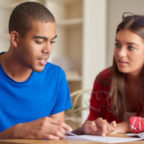 Two university students sat in a classroom.One student is helping the other student.