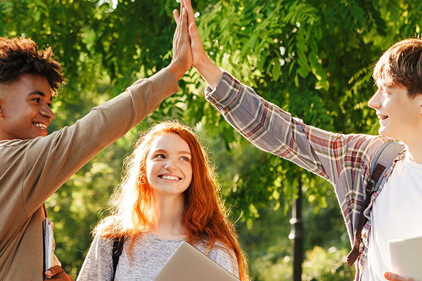 Zwei Teenager klatschen sich ab, ein Mädchen steht lächelnd dabei.
