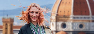 Eine junge Frau mit wehendem Haar lächelt in die Kamera. Im Hintergrund ist Florenz mit dem Dom zu erkennen.