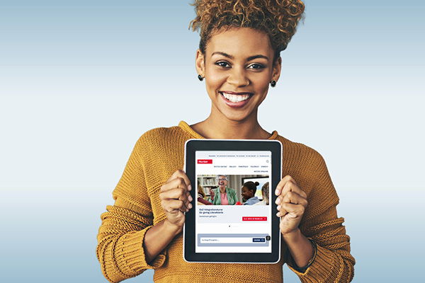 Eine afroamerikanische Frau hält ein Tablet mit der Hueber Homepage in der Hand und lächelt in die Kamera.