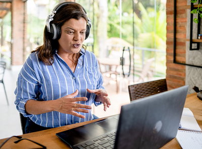 Eine Frau sitzt zuhause mit Kopfhörern vor einem Laptop und spricht in die Kamera.