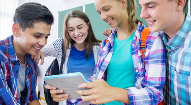 Eine Gruppe Jugendlicher schaut interessiet gemeinsam in ein Tablet.
