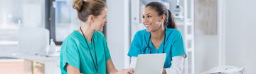 Zwei junge Pflegekräfte sitzen vor einem Laptop und unterhalten sich