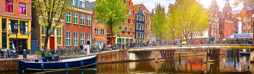 Häuserzeile in Amsterdam mit einem Kanal und einer Brücke davor.